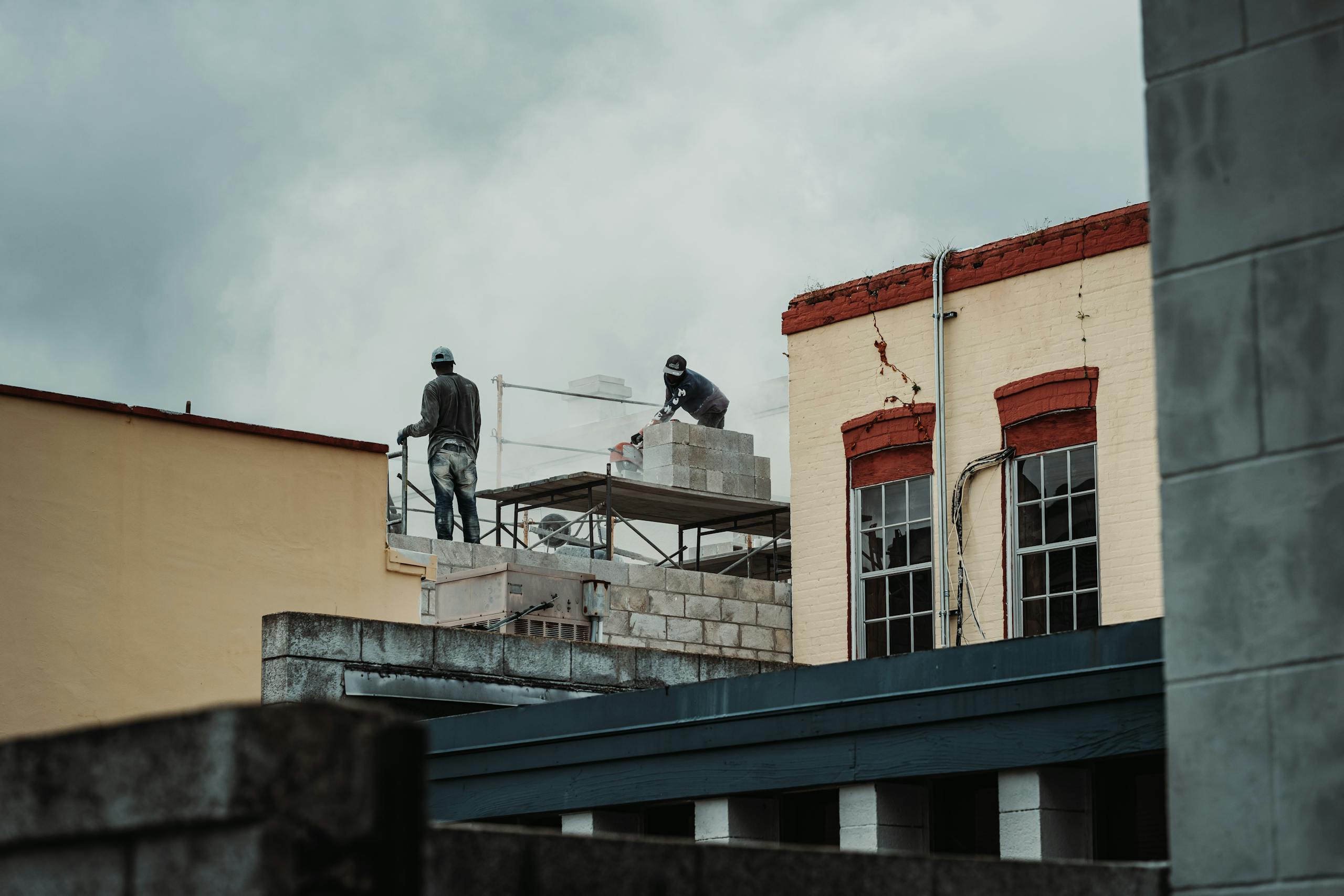 Urban construction scene with workers laying bricks on a building site, captured during the day.