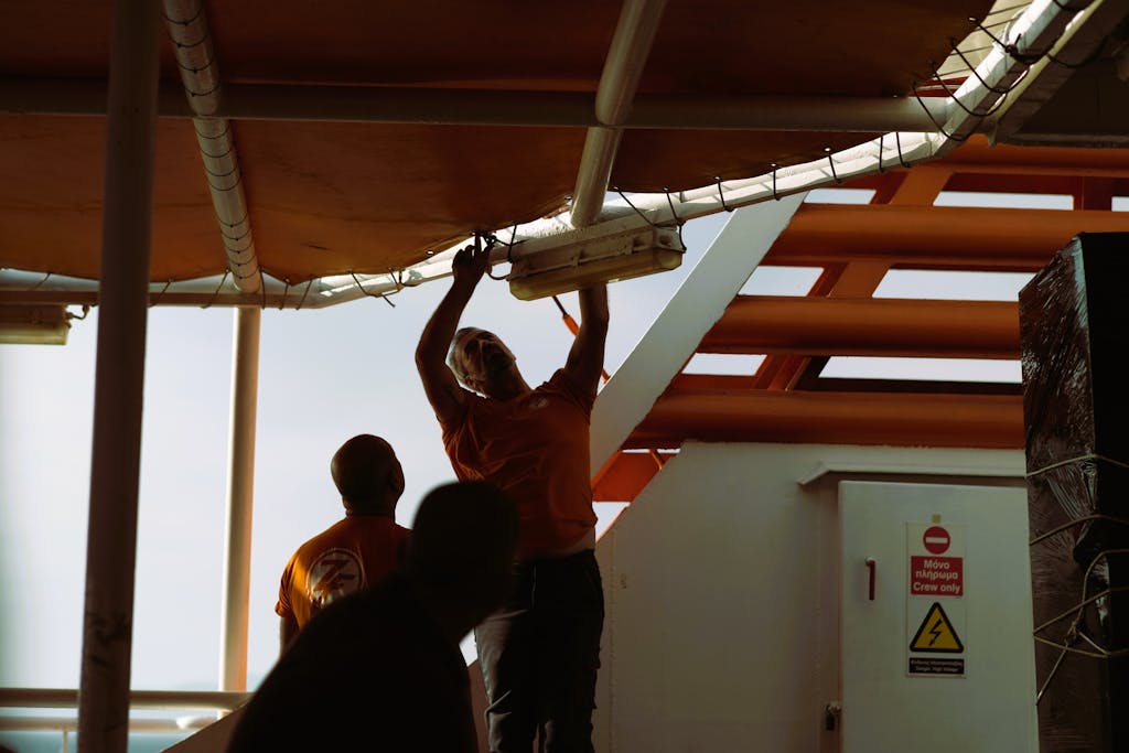 Workers on a ferry in Samothraki, Greece, adjusting lighting fixtures during the day.